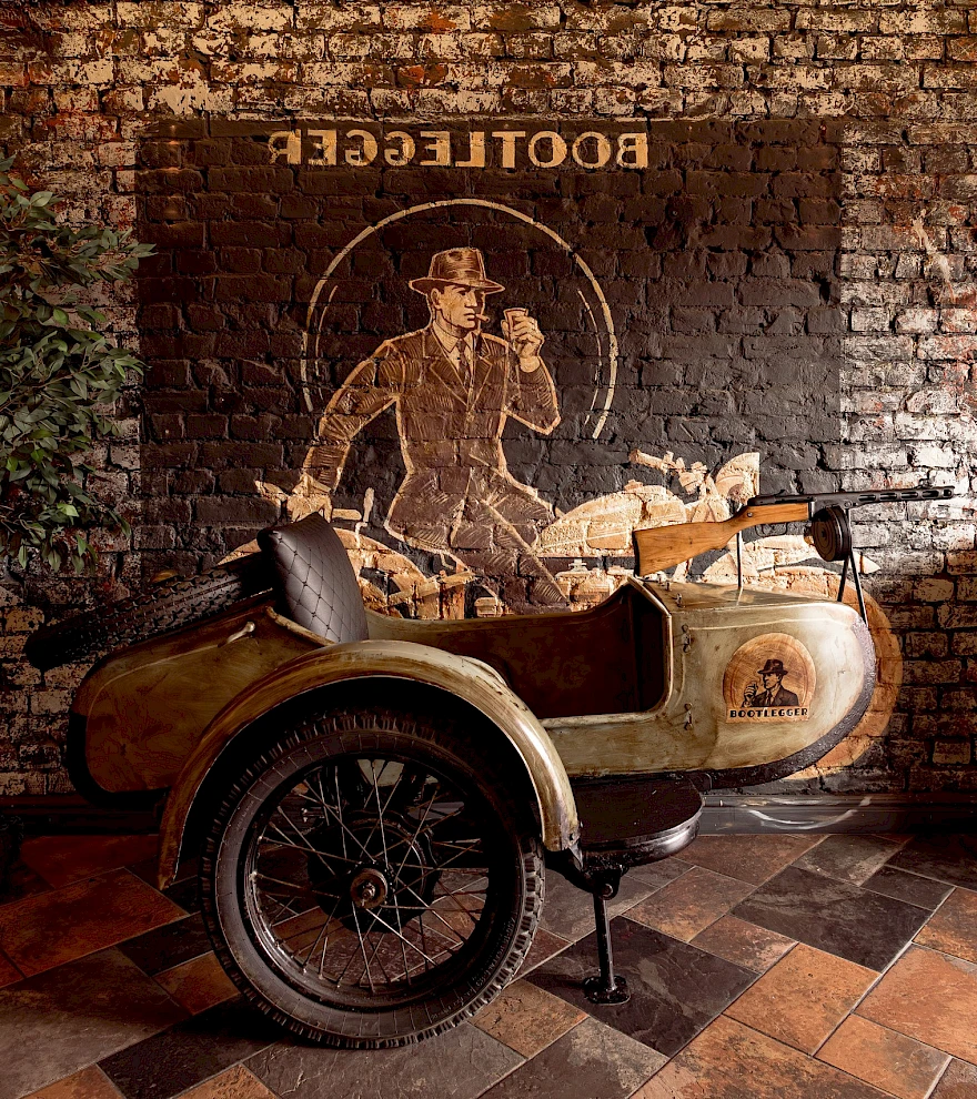 Мотоцикл с коляской у кирпичной стены с муралом OLD BOOTLEGGER